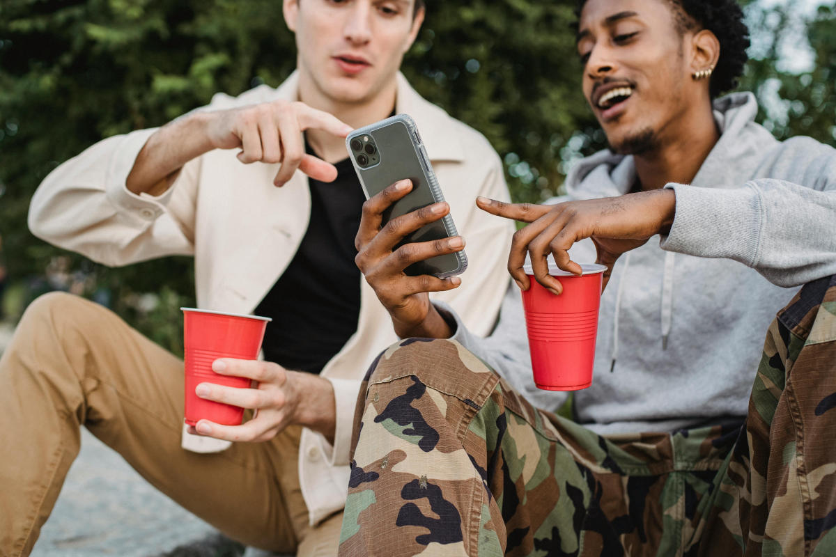 2 Männer zeigen auf ein Handy und trinken aus roten Bechern