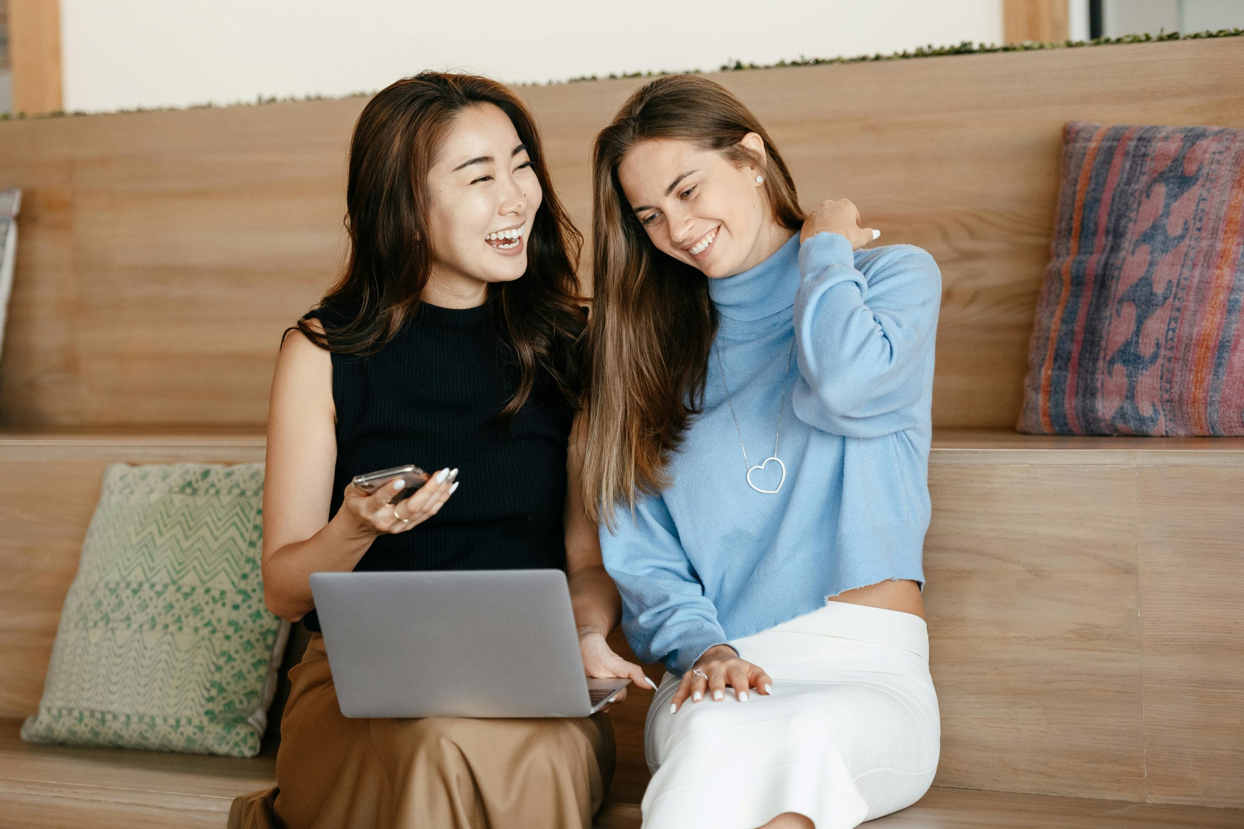 Zwei Personen sitzen vor einem Laptop und lachen